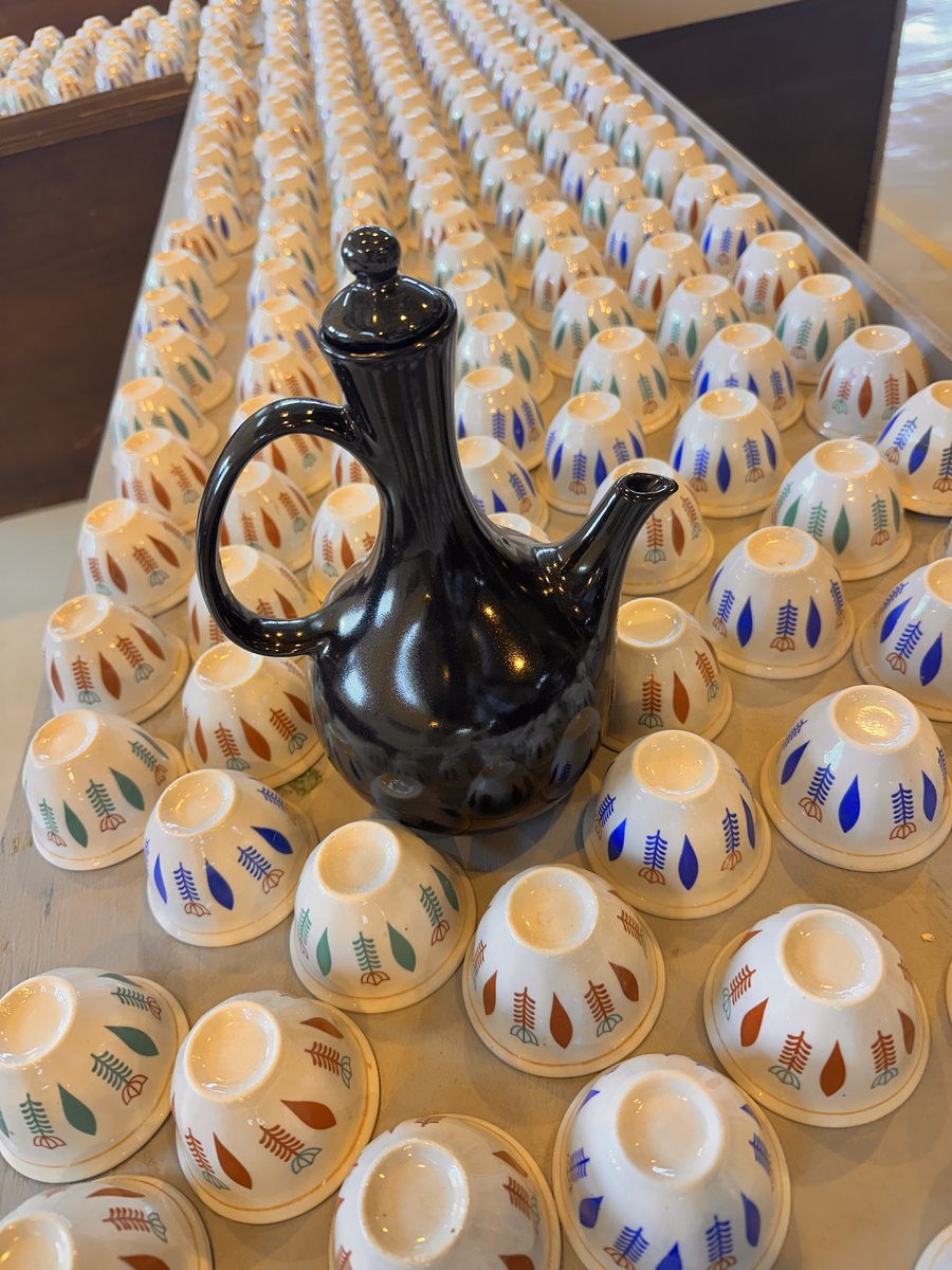 Black jebena coffee pot surrounded by rows of small cups